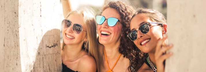 Three people wearing sunglasses smiling closely together outdoors
